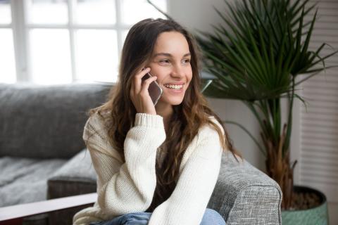 Junge Frau sitzt auf einem Sofa und telefoniert mit dem Smartphone
