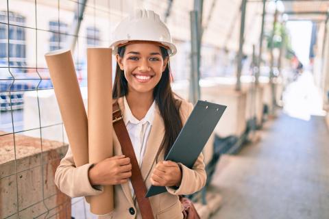 Junge Ingenieurin mit Plänen in der Hand auf einer Baustelle