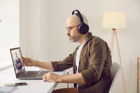 Mann sitzt vor einem Laptop und hat Kopfhörer auf