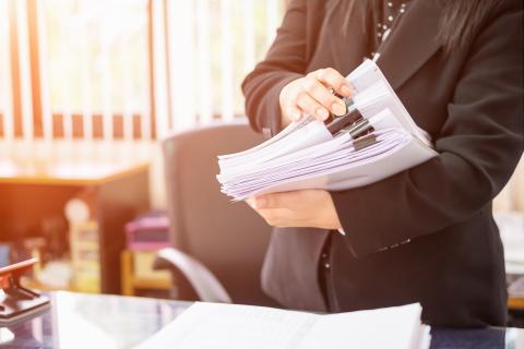 Mann steht hinter seinem Schreibtisch und hat einen großen Stapel verschiedener Ausdrucke in der Hand