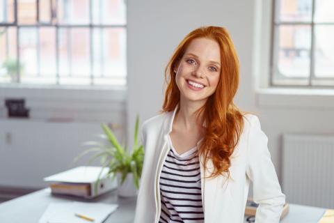 Rothaarige Frau steht in einem Büro vor ihrem Schreibtisch