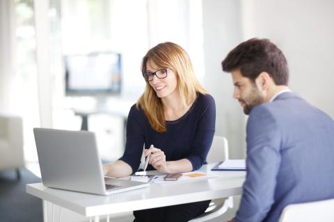Weibliche Führungskraft erläutert einem Mitarbeitenden etwas am Laptop